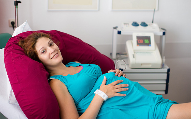 Pregnant woman reclines on a hospital bed holding her bump