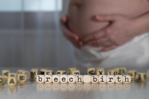 The words breech birth composed of wooden letters. Pregnant woman in the background