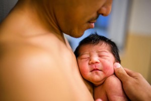 Side view of father holding him newborn baby skin-to-skin