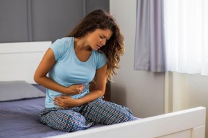 Woman in pain sitting on bed holding her tummy